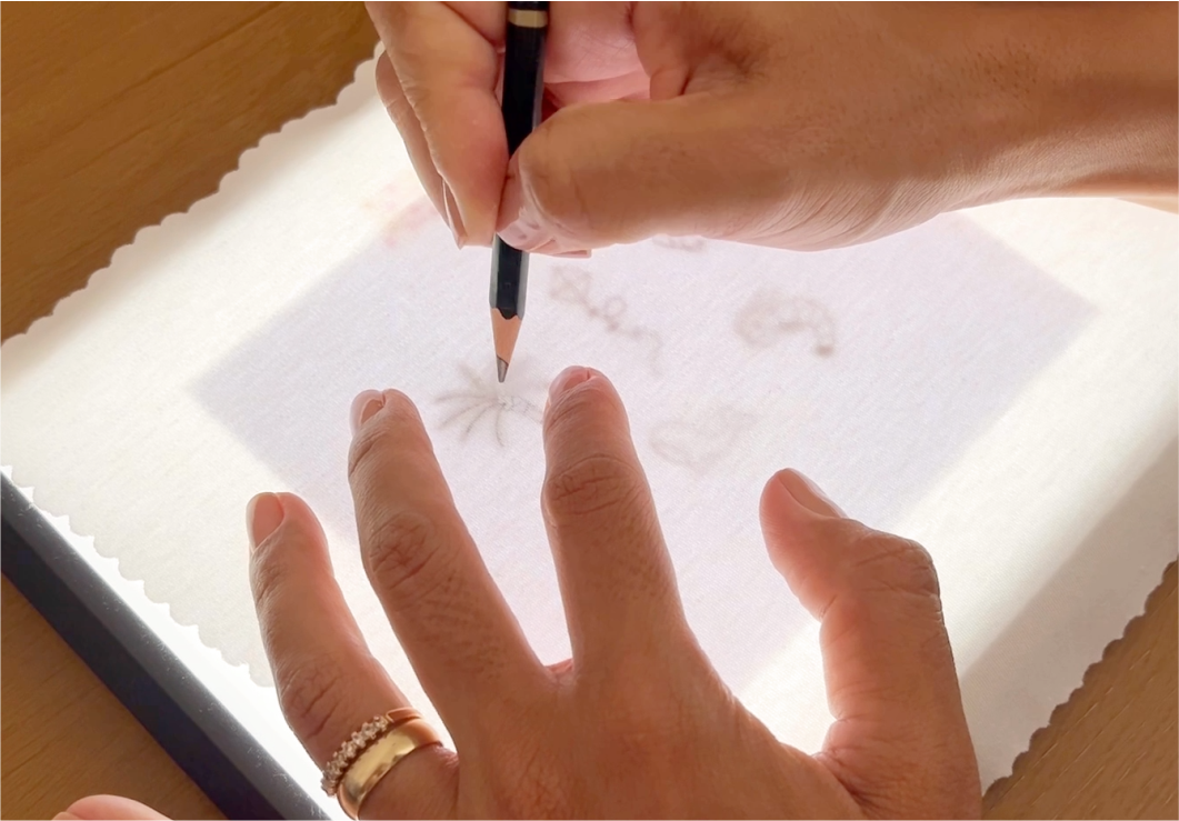 Mãos transferindo um desenho para o tecido com lápis.