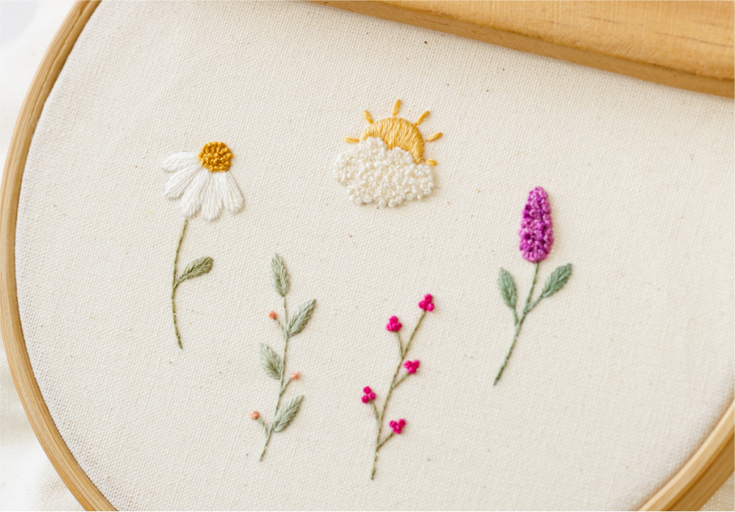 Bastidor com flores, folhas e um sol bordados em diferentes pontos.