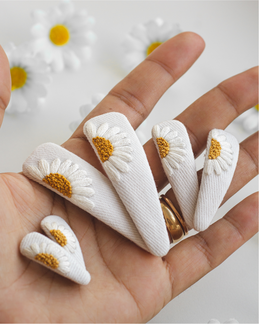 Presilhas de tecido com margaridas bordadas sobre a mão.