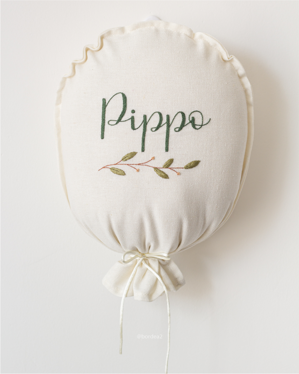 Balão decorativo de tecido com o nome Pippo e folhagens bordadas.