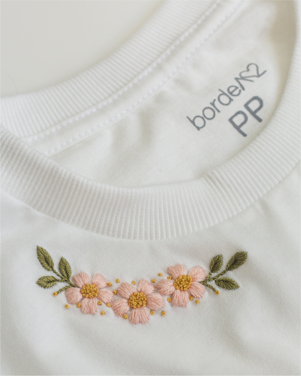 Camiseta branca com pequenas flores bordadas próximas à gola.
